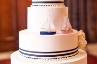 a vintage-inspired nautical wedding cake with navy stripes, pearls, white and pink blooms and two boats instead of a usual topper
