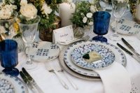 a vintage-inspired nautical wedding tablescape with a crochet tablecloth and napkins, blue patterned plates, neutral blooms and candles