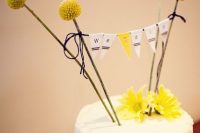 a white buttercream wedding cake with billy balls, a bunting as a topper and yellow blooms is ideal for a rustic wedding