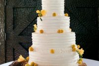 a white buttercream wedding cake with billy balls and yellow blooms plus a metal monogram on top is chic