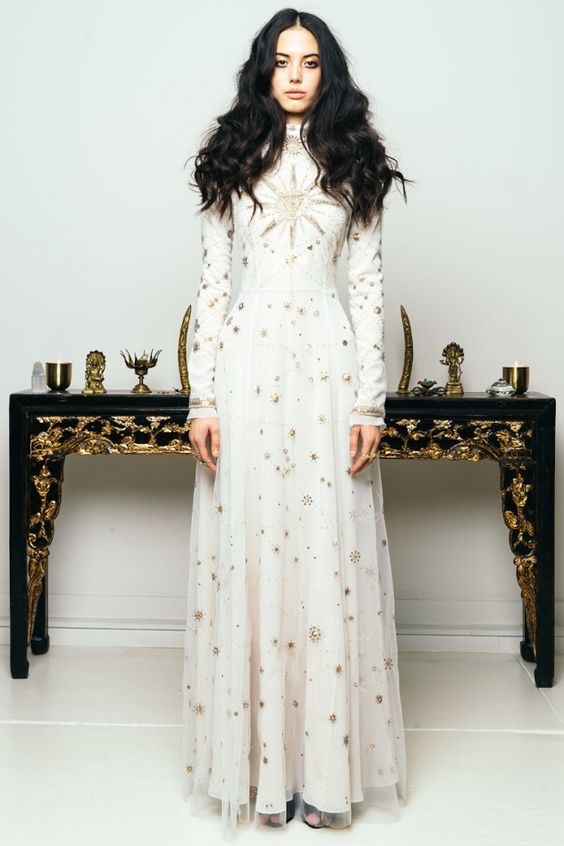 a white sheath wedding dress with a turtleneck, long sleeves, a pleated skirt and gold stars embroidered all over the gown