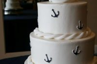 a white wedding cake with ropes, navy anchors, a white and anavy anchor on top, with a veil and a bow is amazing