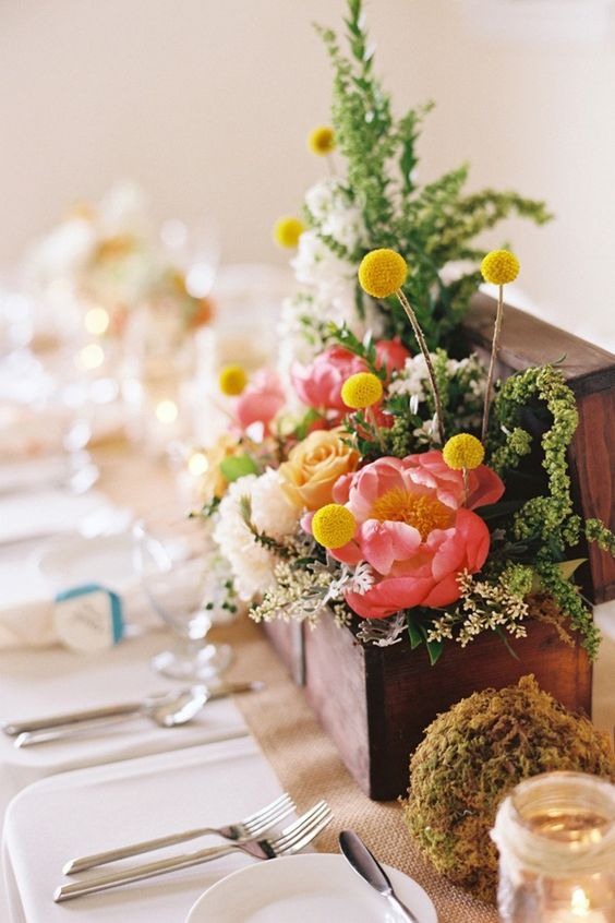 a wooden box with greenery, coral and peachy and white blooms, billy balls and a moss ball is a cool idea to rock