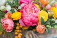 21 a colorful wedding bouquet with bright pink peonies, yellow and orange ranunculus, berries and white blooms and lots of greenery