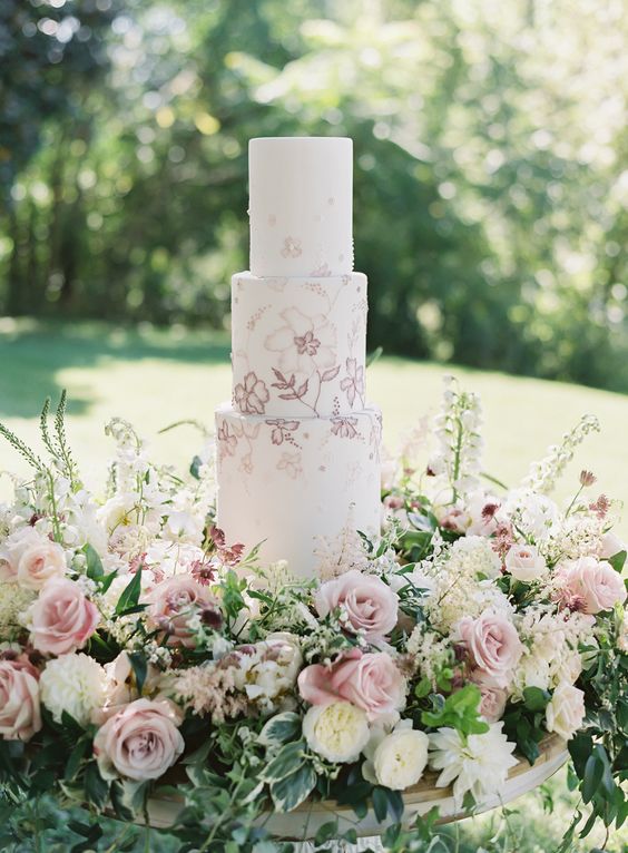 a delicate secret garden wedding cake with pink and mauve blooms painted and lush blooms around is amazing