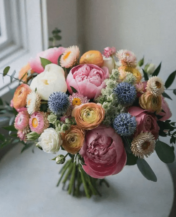 a beautiful and delicate wedding bouquet with yellow ranunculus, white and pink peonies, allium and some dried blooms