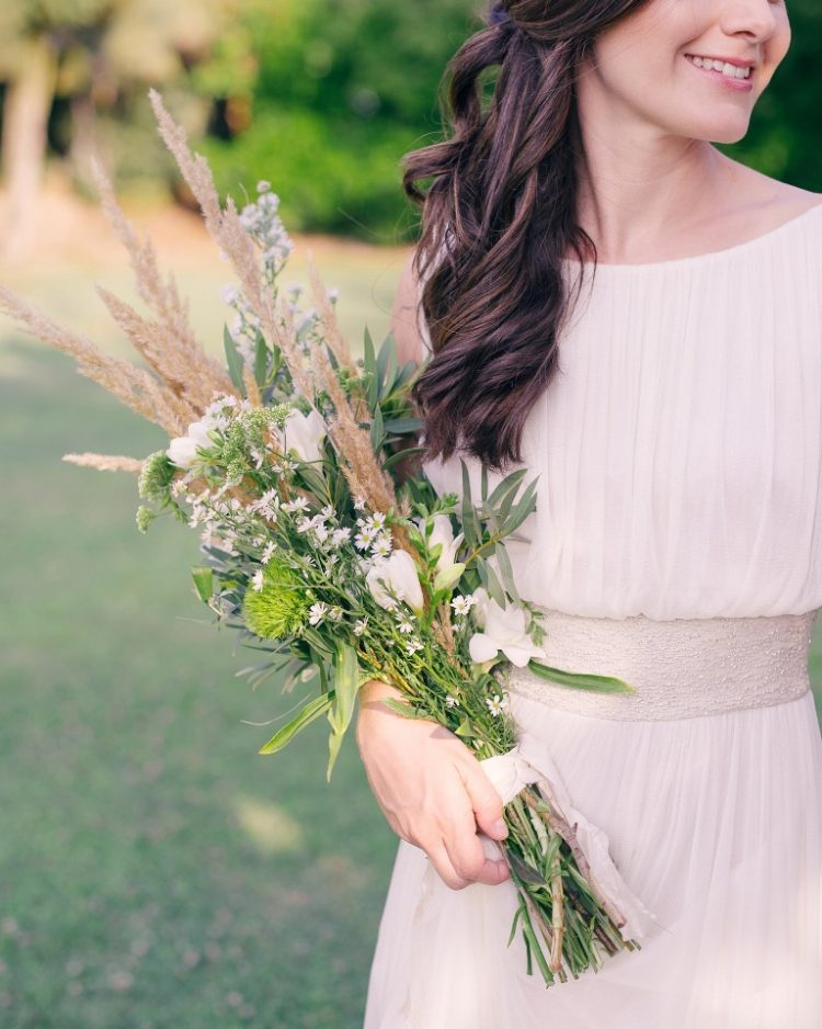 a beautiful and textural long stem wedding bouquet with white blooms, green ones, greenery, dried grasses and white ribbons