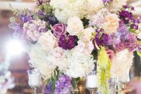 a beautiful and unusual secret garden wedding centerpiece of candles, white, purple and lilac blooms and greenery