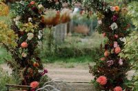 a beautiful secret garden wedding arch covered with leaves, blush, white, deep and bright red blooms is a very chic and bold idea for fall