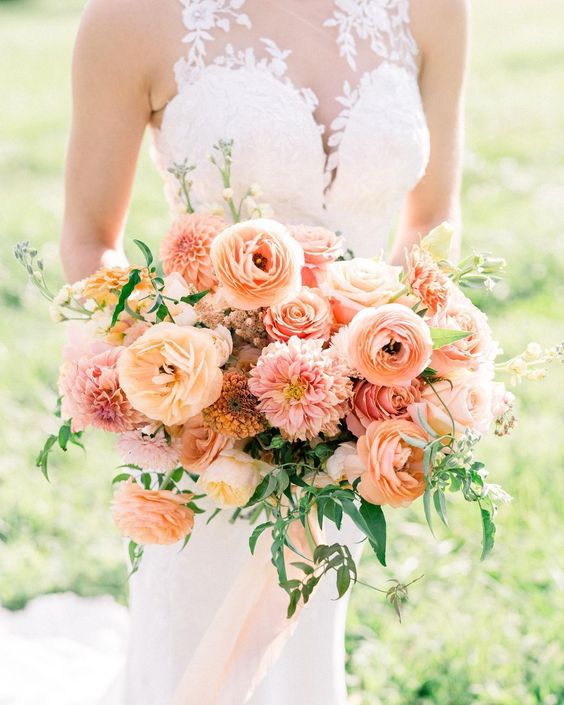 A beautiful sunset colored wedding bouquet with peachy and blush blooms including dahlias and ranunculus and greenery