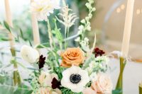 a beautiful wedding centerpiece with blush and rust roses, white ranunculus and anemones, greenery and elegant tall candles