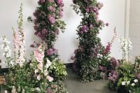 a beautiful wedding ceremony space with an arch made of greenery and lilac, with greenery and blooms around feels like a real indoor garden