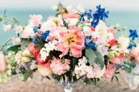 a bright secret garden wedding centerpiece of a glass bowl, bold pink and blue blooms and some foliage is chic and amazing