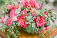 a bright statement secret garden wedding centerpiece of hot pink peonies, pink ranunculus and greenery plus some thistles