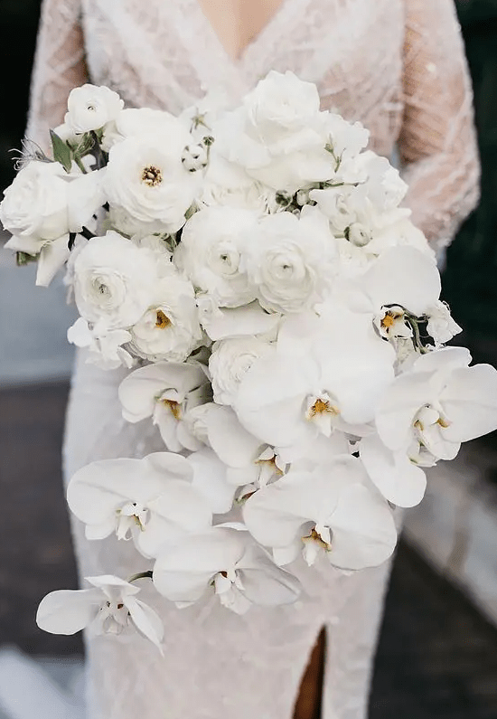 a cascading white wedding bouquet of ranunculus and orchids is a beautiful idea for a modern wedding