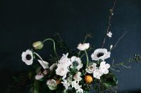 a catchy wedding centerpiece of white anemones and other blooms, greenery, twigs and branches, with some citrus in a clear vase