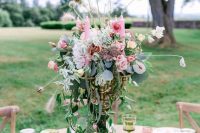 a chic and bright secret garden wedding centerpiece of a tall vase, pink blooms, greenery and seed pods looks very quirky