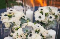 a chic anemone, ranunculus and pale greenery wedding centerpiece with succulents and tall candles in glasses is very cool and up-to-date