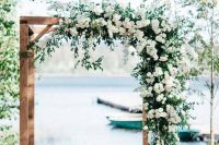 a chic rustic wedding arch of wood, with greenery and white blooms on top is a very stylish and beautiful idea for any season