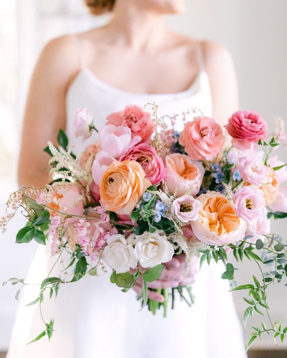 a chic wedding bouquet of pink and orange ranunculus, peachy peony roses, fillers and white roses is cool for spring