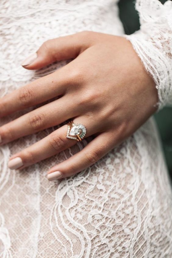 a chic white pear-shaped diamond wedding ring in a stack with a triangle mini diamond one and a lower arched ring with diamonds