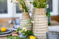 a cluster wedding centerpiece of woven vases with daisies and greenery, wooden beads and lemons on the table