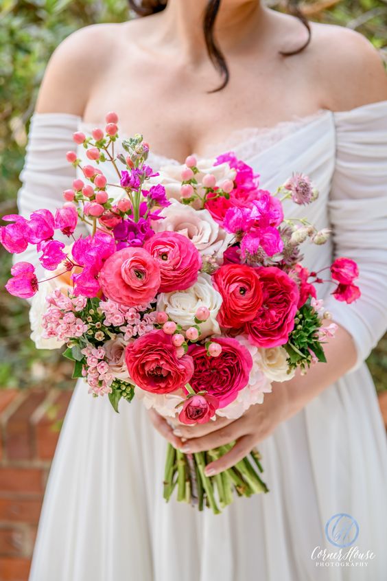 a colorful ranunculus wedding bouquet with pink, red and hot pink blooms, white roses and some fillers