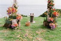 a colorful rustic wedding arch of birch branches, greenery and colorful blooms, petals on the ground and a sea view