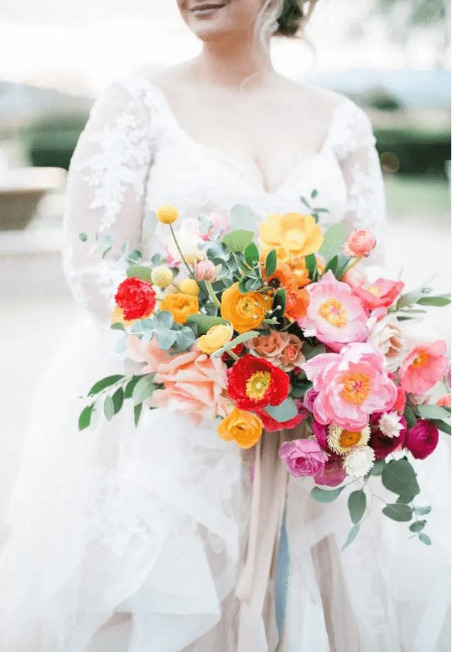 a colorful wedding bouquet of pink peonies, hot pink and yellow ranunculus, billy balls, some yellow and red poppies and greenery