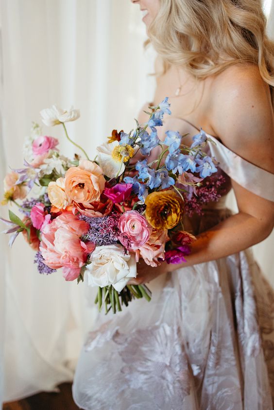 a colorful wedding bouquet with pink peonies, orange, pink and mustard ranunculus and some smaller fillers