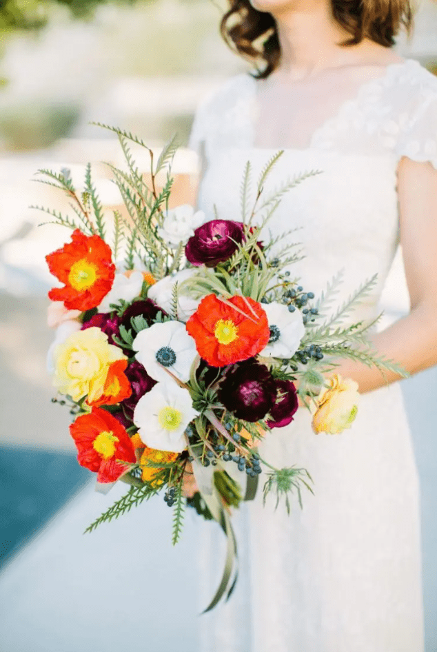 a contrasting wedding bouquet of white and red poppies and anemones, yellow and purple ranunculus, greenery and berries