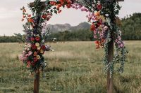 a cool rustic wedding arch of stained wood, greenery and bright blooms is a lovely solution for a summer wedding