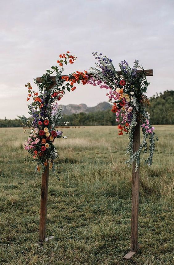 a cool rustic wedding arch of stained wood, greenery and bright blooms is a lovely solution for a summer wedding