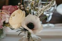 a creative and small wedding centerpiece of a bottle, a white ranunculus and anemone, berries and astilbe is a chic idea for spring or summer