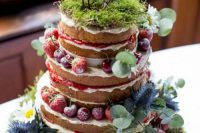 a creative enchanted forest naked wedding cake with fresh berries, moss, greenery, bird toppers on a moss pillow with greenery