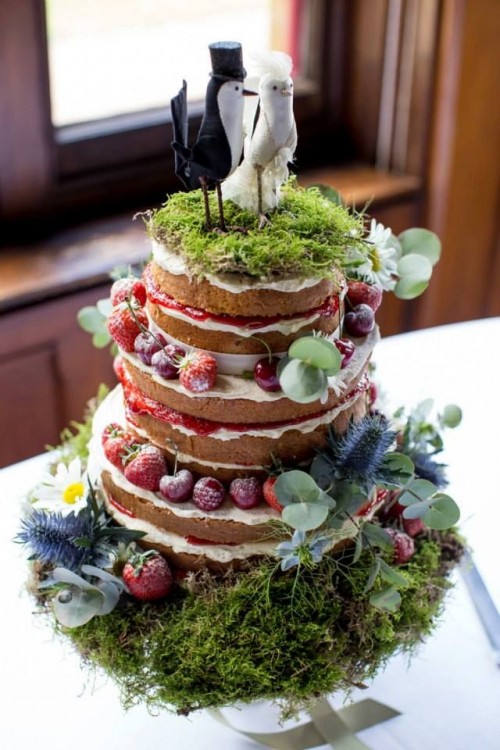 a creative enchanted forest naked wedding cake with fresh berries, moss, greenery, bird toppers on a moss pillow with greenery