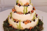 a creative enchanted forest wedding cake in white, with sugar foliage, mushrooms and nuts placed on a moss pillow