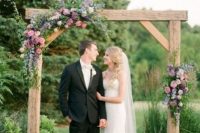 a cute summer rustic wedding arch of wood, greenery, mauve and pink blooms is a cool idea for a rustic summer wedding