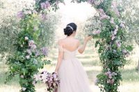 a dreamy garden wedding arch with greenery and lilac is a chic idea that looks incredibly romantic and very beautiful