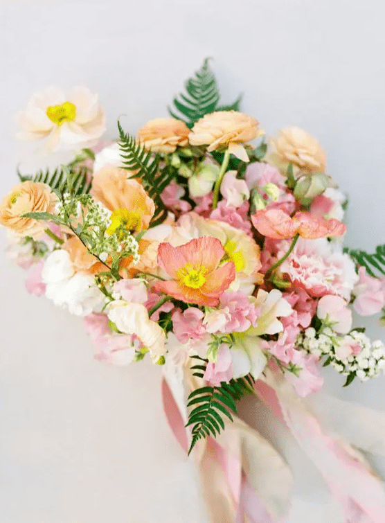 a dreamy pastel wedding bouquet of pink and yellow poppies, yellow and pink ranunculus, greenery and long ribbon is wow