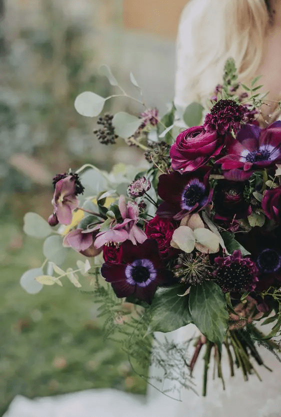 a fantastic wedding bouquet with purple anemones and ranunculus, deep purple blooms, berries and greenery for a moody wedding