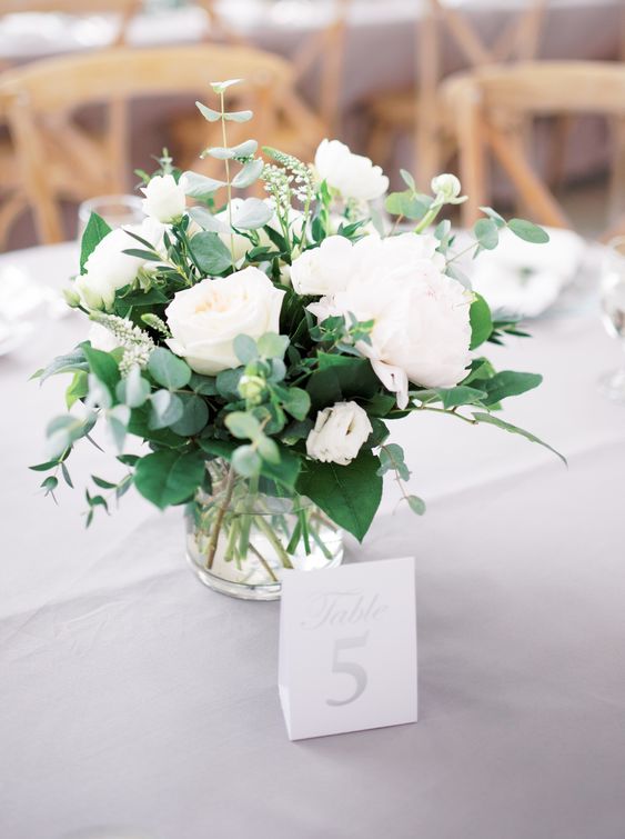 a fresh and stylish wedding centerpiece of various types of greenery, white peonies in a sheer vase is a lovely idea