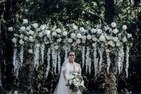 a gorgeous and very lush wedding arch covered with foliage and lots of white blooms on top and hanging down