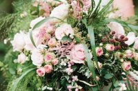 a gorgeous secret garden wedding centerpiece with lots of greenery and grasses, lots of pink blooms and berries is amazing for summer