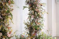 a jaw-dropping garden wedding arch covered with greenery, yellow, blush and white blooms and some arrangements at the base looks fantastic