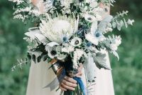a lovely and chic long stem wedding bouquet with a white king protea and smaller white blooms, greenert and thistles plus blue ribbons