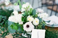 a lovely and fresh wedding centerpiece with white hydrangeas, anemones and ranunculus, greenery and an additional greenery table runner