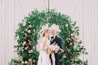 a lovely garden wedding arch decorated with greenery, blush and pink blooms and arrangements at the base looks lush and beautiful