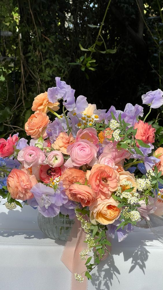 a lovely pastel spring wedding bouquet with lilac sweet peas, pink and orange ranunculus and chamomile plus greenery
