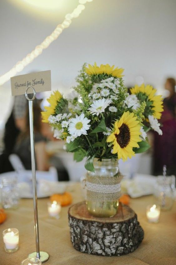 a lovely rustic wedding centerpiece of a jar wrapped in burlap, daisies, sunflowers and some foliage is a cool idea